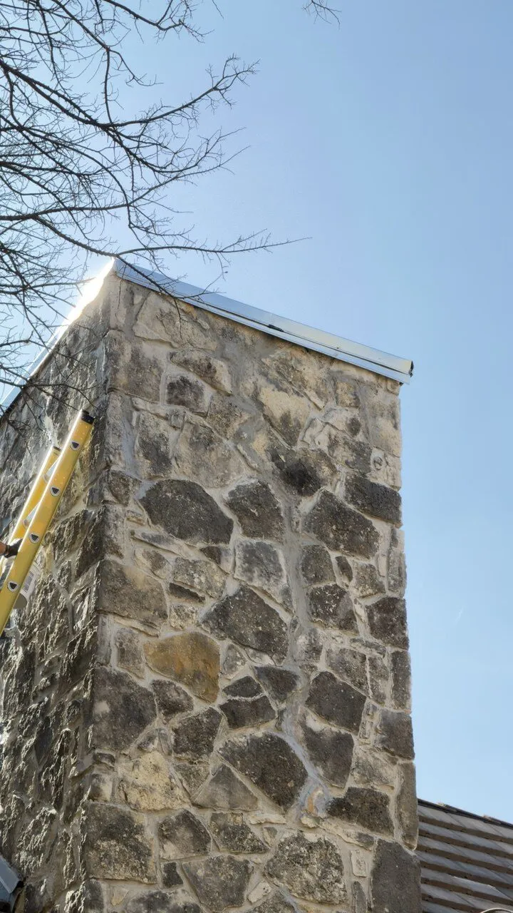 Technician on the ladder documenting a stone chimney before repair